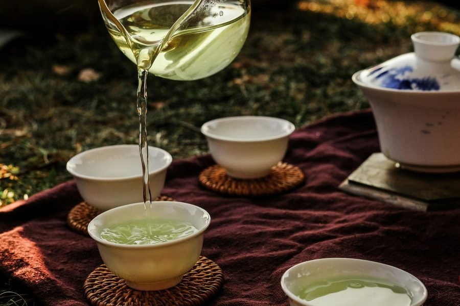 Pouring green tea from a fairness pitcher into tasting cups beside a gaiwan.