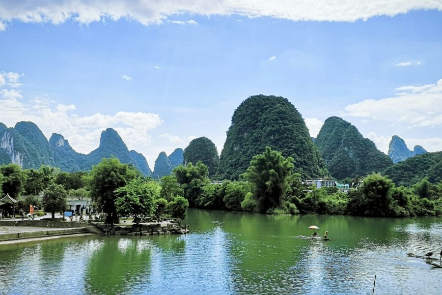 Bamboo rafts gliding on a green river below karst hills under a bright summer sky in Yangshuo.