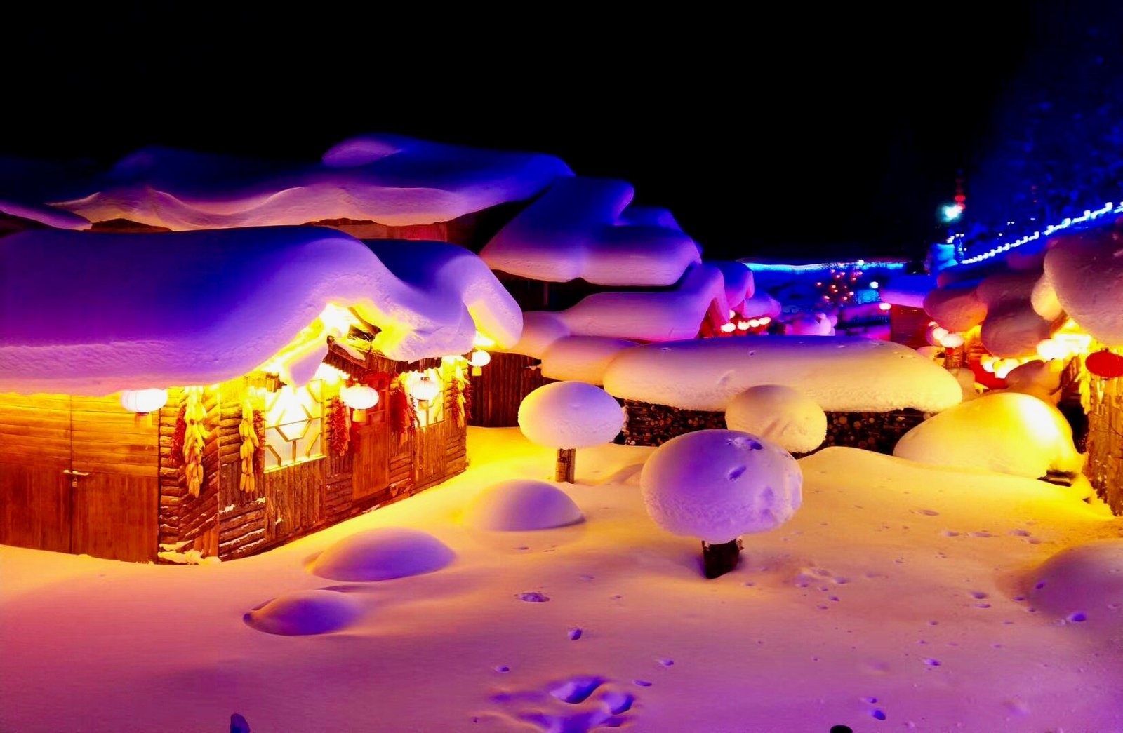 Snow-covered wooden cabins in China Snow Town illuminated by warm lanterns at night