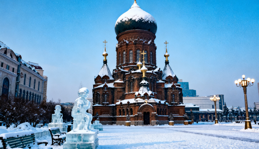 A snow - covered square with the Saint Sophia Cathedral at its center, surrounded by ice sculptures, snow - laden benches, and street lamps under a clear blue sky.